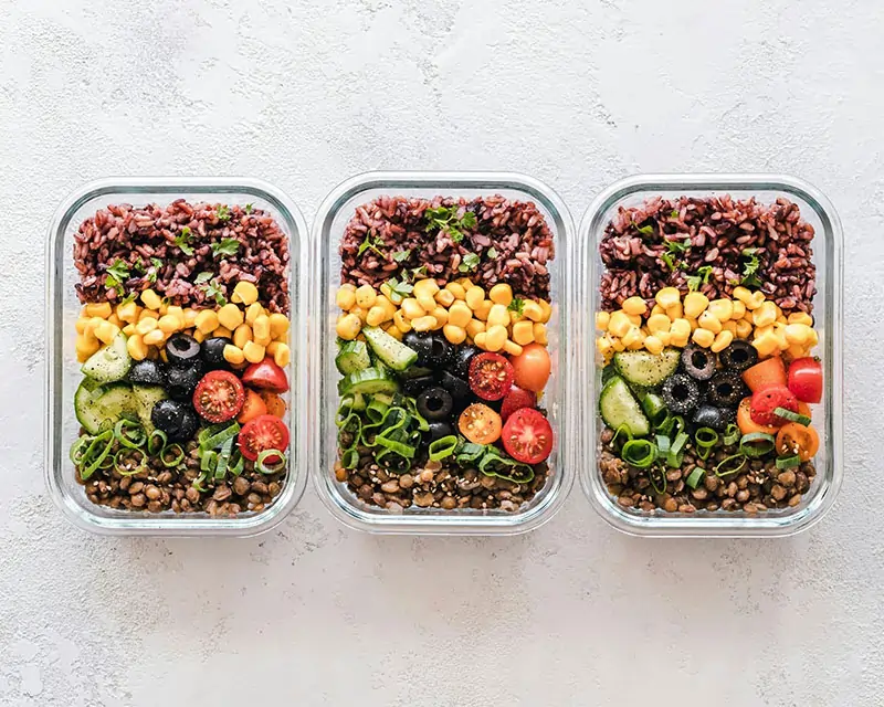 Colorful Meal Prep Bowls with Rice, Corn, Cucumbers, Olives, and Cherry Tomatoes Neatly Arranged